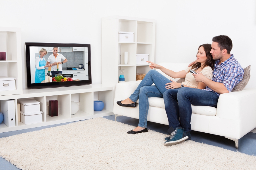 Young Couple Sitting On Couch Watching Cookery Show