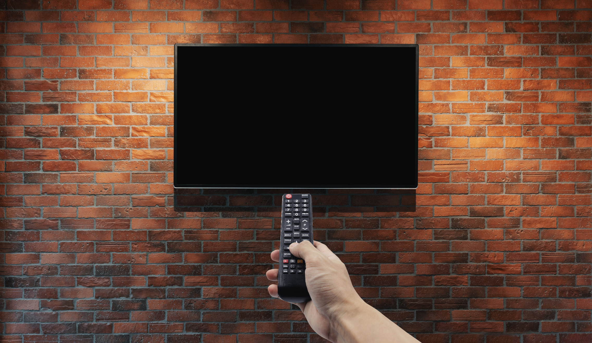 Television on brick wall with hand using remote control