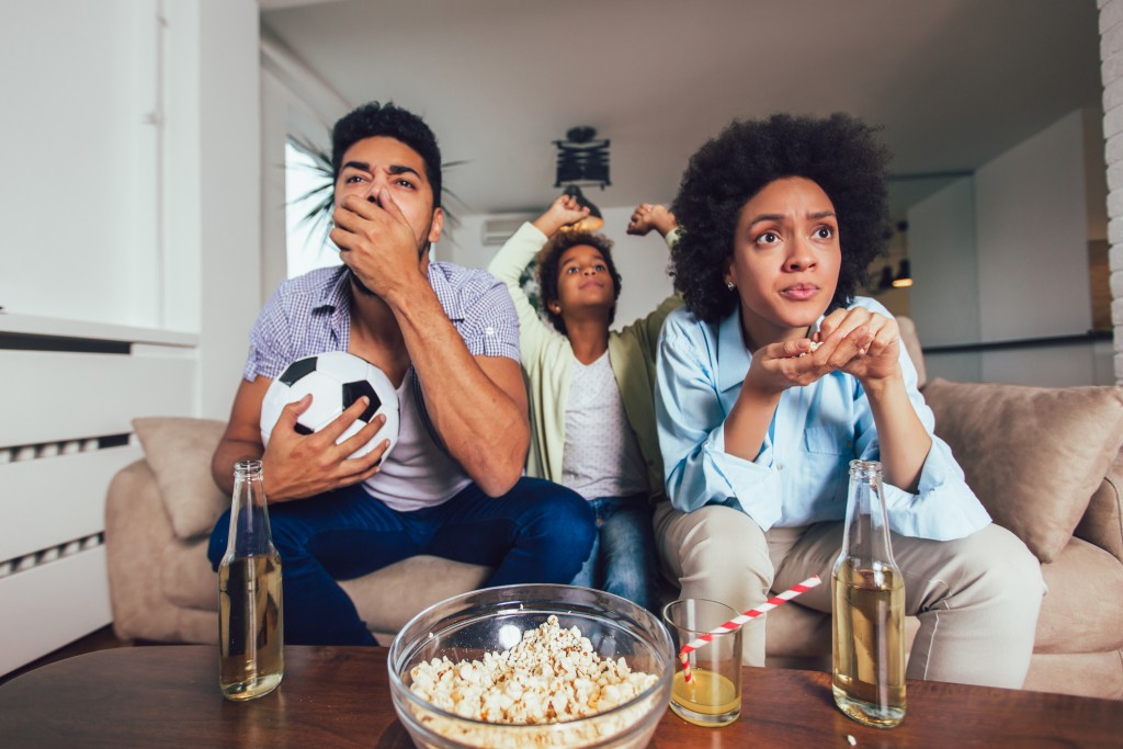 Happy family of three watching tv and cheering sport games on sofa at home