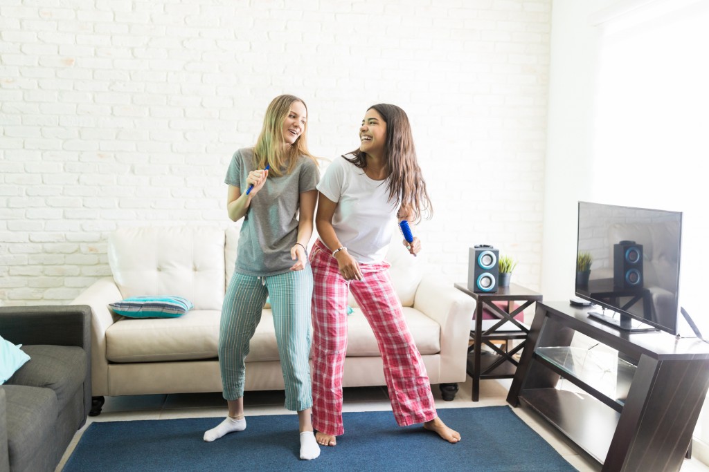 Full length of cheerful women singing karaoke and dancing in living room