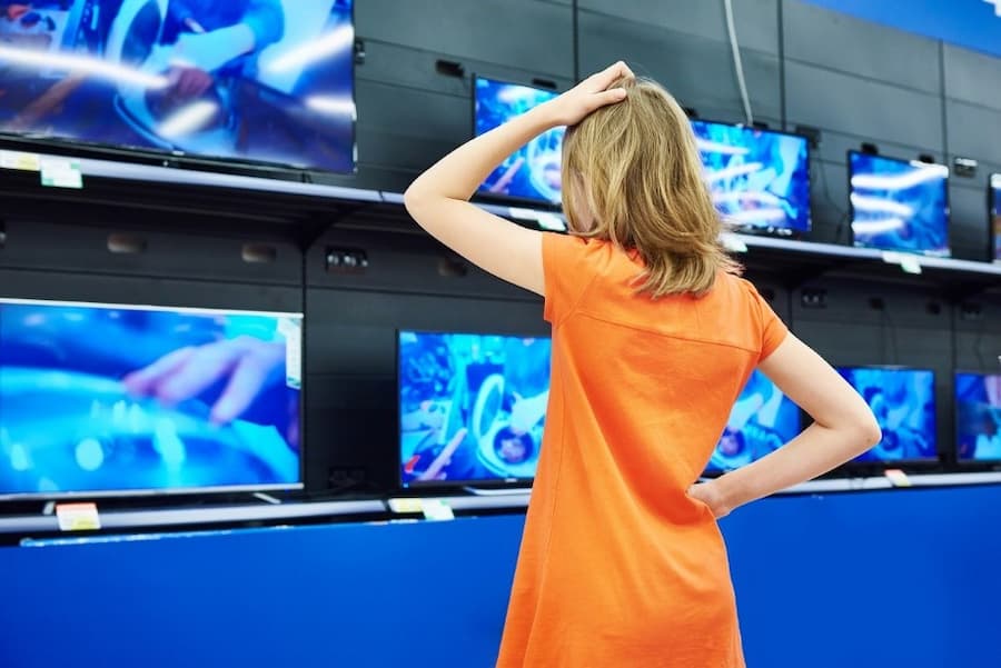 A person in an orange dress looking at a wall of televisions